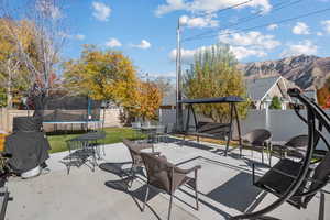 Fenced backyard featuring a trampoline, outdoor dining space, a patio, a mountain view, and a grill