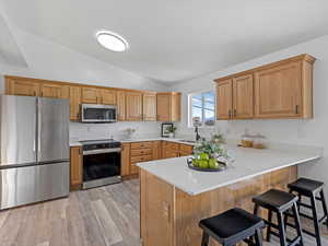 Kitchen featuring appliances with stainless steel finishes, a kitchen breakfast bar, light wood-type flooring, vaulted ceiling, and a peninsula