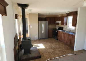 Kitchen featuring a wood stove, freestanding refrigerator, electric range, dark countertops, and under cabinet range hood