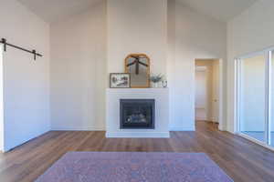 Unfurnished living room with a barn door, a glass covered fireplace, high vaulted ceiling, and dark wood-style flooring