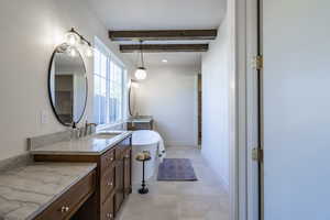 Bathroom featuring a soaking tub, two vanities, and beamed ceiling
