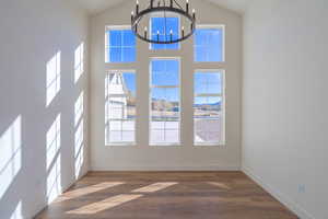Unfurnished dining area with a chandelier, dark wood-style floors, and high vaulted ceiling