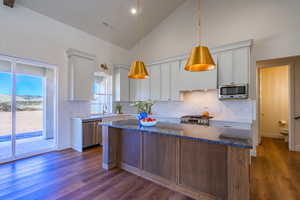 Kitchen with high vaulted ceiling, backsplash, white cabinetry, dark stone countertops, and dark wood-style flooring