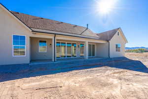 Back of house featuring a patio area, a shingled roof, and stucco siding
