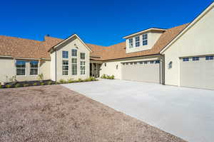 View of front facade featuring roof with shingles, concrete driveway, stucco siding, and a garage