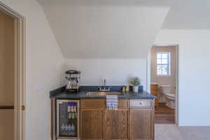 Indoor wet bar featuring dark countertops, wine cooler, and brown cabinetry