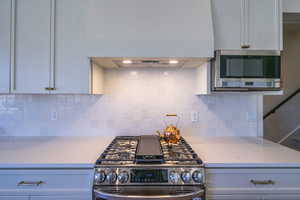 Kitchen featuring appliances with stainless steel finishes, under cabinet range hood, decorative backsplash, and light stone countertops