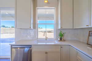 Kitchen with dishwasher, white cabinetry, decorative backsplash, and light stone counters
