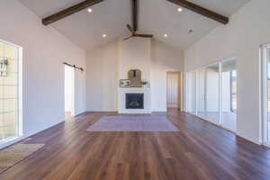 Unfurnished living room featuring a barn door, high vaulted ceiling, a ceiling fan, beamed ceiling, and a fireplace