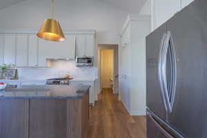 Kitchen featuring appliances with stainless steel finishes, white cabinetry, dark wood-style flooring, decorative backsplash, and dark stone counters