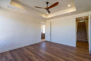 Unfurnished bedroom with a tray ceiling, connected bathroom, dark wood-type flooring, a ceiling fan, and recessed lighting