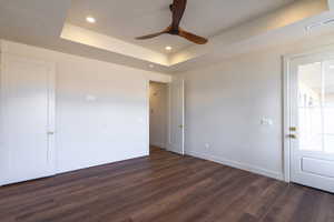 Spare room with a raised ceiling, dark wood-type flooring, recessed lighting, and ceiling fan