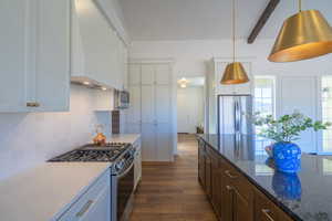 Kitchen with appliances with stainless steel finishes, custom exhaust hood, dark wood-style floors, decorative backsplash, and dark stone counters