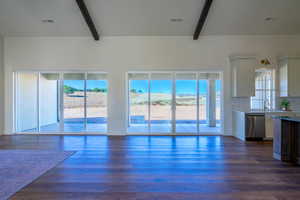 Unfurnished living room featuring beam ceiling, dark wood-type flooring, and a high ceiling