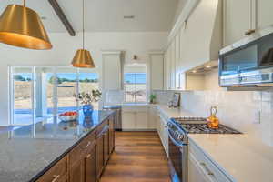 Kitchen with stainless steel appliances, decorative backsplash, dark wood-style flooring, beam ceiling, and dark stone countertops