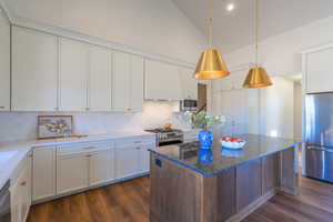 Kitchen with dark wood-type flooring, white cabinets, stainless steel appliances, a center island, and vaulted ceiling