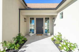 Doorway to property with covered porch, roof with shingles, and stucco siding