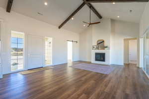 Unfurnished living room featuring beam ceiling, a barn door, high vaulted ceiling, recessed lighting, and dark wood-style flooring