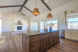Kitchen with beam ceiling, high vaulted ceiling, a kitchen island, dark stone countertops, and dark wood-style flooring