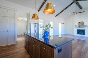 Kitchen featuring beam ceiling, dark brown cabinetry, a barn door, dark wood-type flooring, and dark stone counters