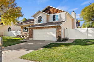 Traditional-style house featuring concrete driveway, an attached garage, a gate, brick siding, and a chimney