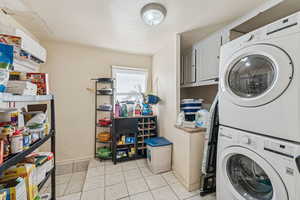 Laundry area with light tile patterned floors, stacked washer / drying machine, and cabinet space