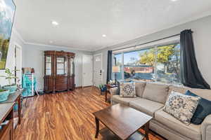 Living room with ornamental molding, wood finished floors, a textured ceiling, and recessed lighting