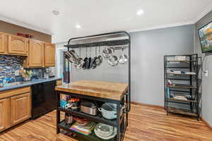 Kitchen with decorative backsplash, crown molding, light wood-type flooring, black dishwasher, and recessed lighting