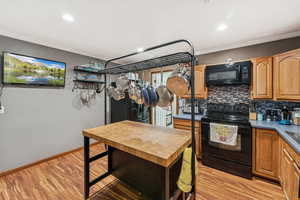 Kitchen featuring black appliances, crown molding, backsplash, light wood-style flooring, and recessed lighting
