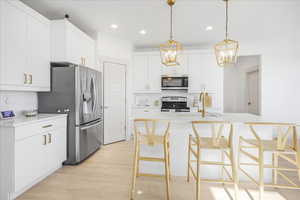 Kitchen featuring white cabinets, light wood-style floors, stainless steel appliances, hanging light fixtures, and recessed lighting