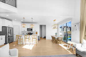 Living area with recessed lighting, light wood-style floors, a chandelier, and a towering ceiling