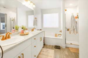 Bathroom with double vanity, light wood-style floors, a stall shower, and a garden tub