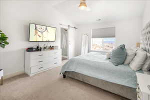 Bedroom featuring a barn door, lofted ceiling, light colored carpet, and ensuite bathroom