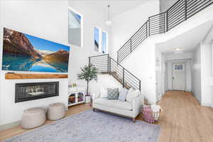 Living area featuring a high ceiling, light wood-style flooring, stairs, and a glass covered fireplace