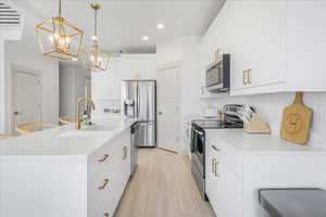 Kitchen featuring white cabinetry, appliances with stainless steel finishes, a kitchen island with sink, pendant lighting, and light wood-type flooring