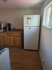 Kitchen with freestanding refrigerator, dark wood-style floors, washer / dryer, and brown cabinets