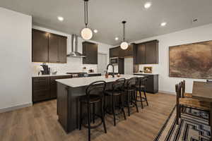 Kitchen with a breakfast bar, a kitchen island with sink, dark wood finish cabinetry, hanging light fixtures, and dark wood-style floors