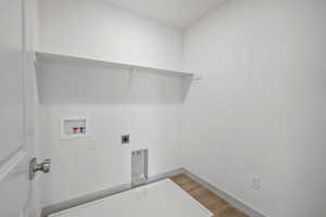 Washroom with hookup for a washing machine, electric dryer hookup, and light wood finished floors