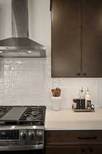 Kitchen with dark wood finish cabinets, gas range, tasteful backsplash, and light stone countertops