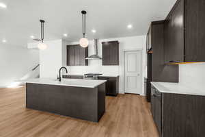 Kitchen with dark brown cabinets, a kitchen island with sink, decorative light fixtures, light wood-type flooring, and backsplash