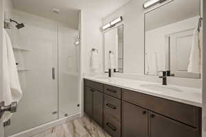 Bathroom featuring double vanity, a shower stall, a textured ceiling, and light marble finish floors
