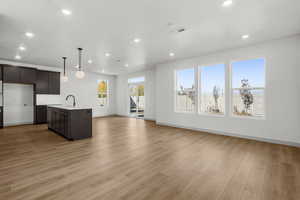 Kitchen with dark brown cabinetry, open floor plan, pendant lighting, a kitchen island with sink, and recessed lighting