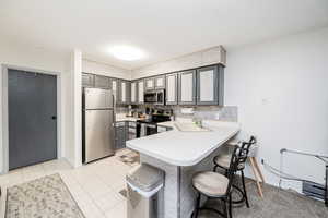 Kitchen with gray cabinetry, a kitchen bar, appliances with stainless steel finishes, and a peninsula