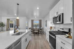 Kitchen featuring stainless steel appliances, white cabinets, light wood-type flooring, pendant lighting, and recessed lighting