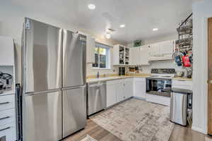 Kitchen with appliances with stainless steel finishes, light countertops, white cabinetry, light wood-type flooring, and recessed lighting