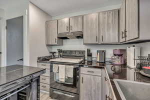 Kitchen with stainless steel range with electric stovetop, under cabinet range hood, and light wood finished floors