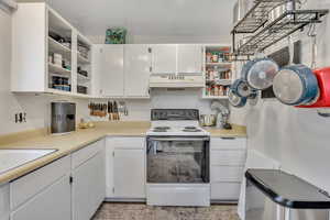 Kitchen with open shelves, electric range, white cabinetry, light countertops, and under cabinet range hood