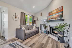Living room featuring vaulted ceiling, wood finished floors, a tiled fireplace, and recessed lighting