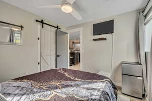 Bedroom with freestanding refrigerator, a barn door, ceiling fan, and light wood-style flooring