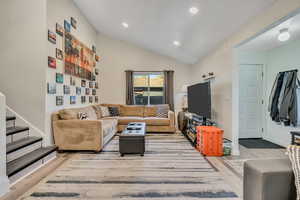 Living room featuring vaulted ceiling, light wood-style flooring, recessed lighting, and stairs